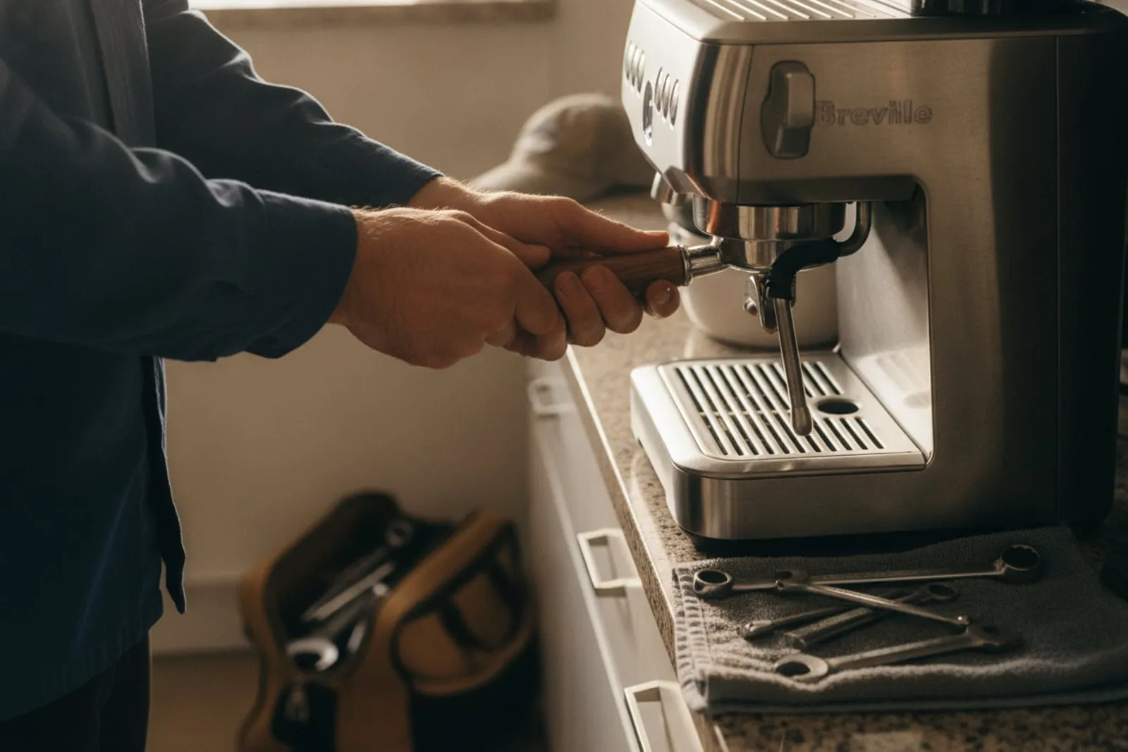 Technician's hands locking a portafilter into the group of a Breville espresso machine, tools on a towel below